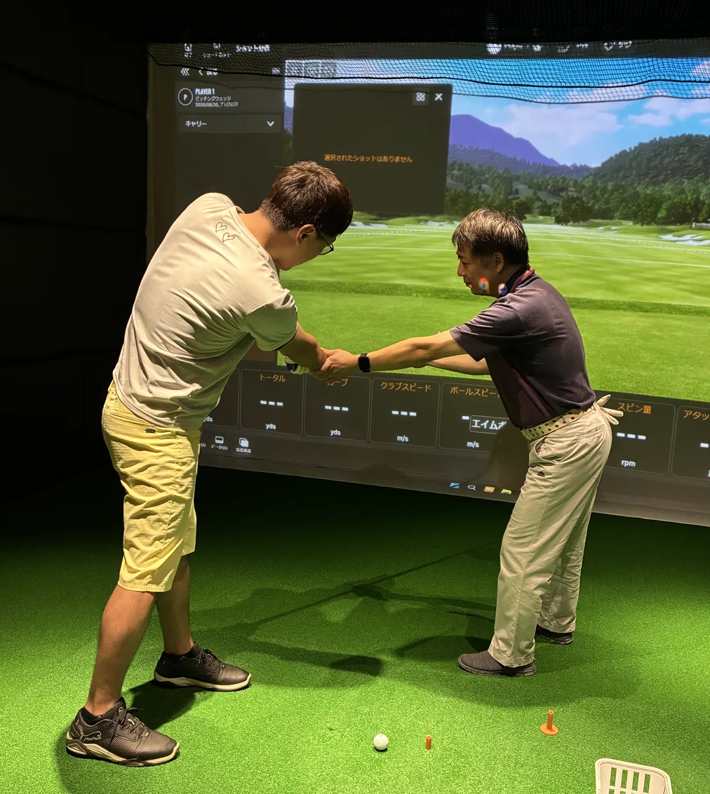 レッスンプロがシミュレーターの前でスイングを指導している様子
